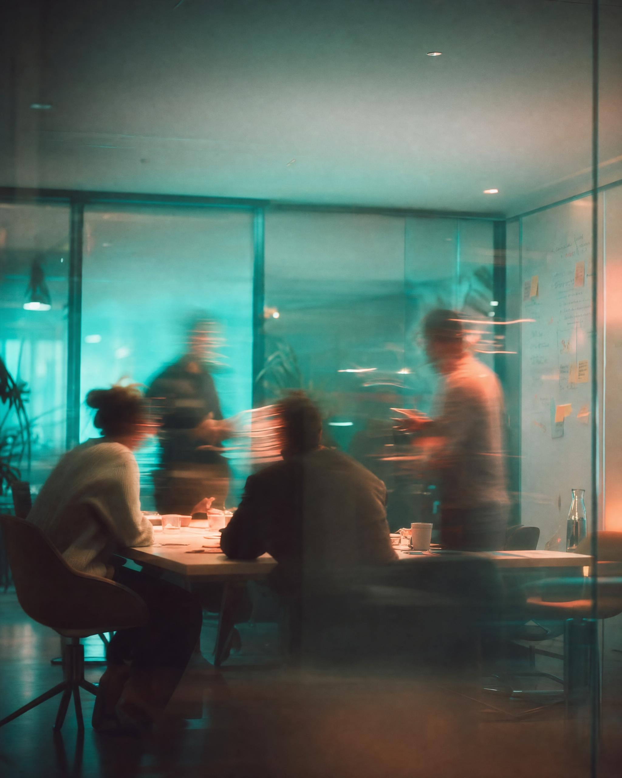 A team meeting in a glass-walled office, seen through motion blur and reflections